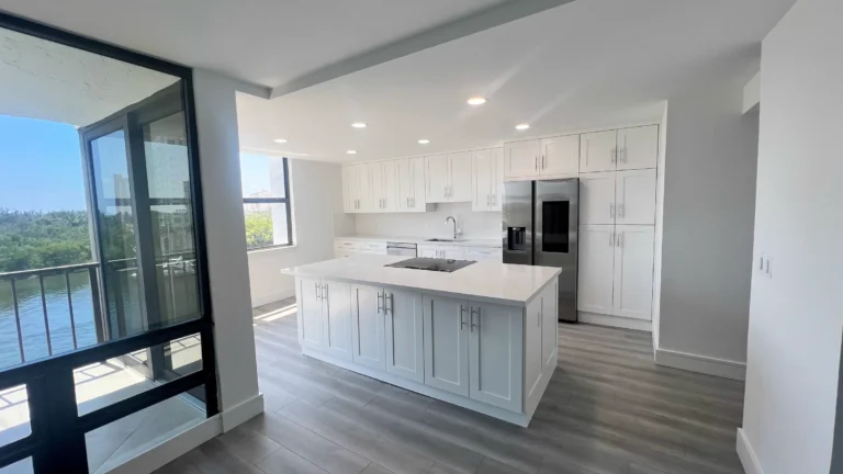 Open white kitchen with a large island, gray wood-look floors and floor-to-ceiling windows