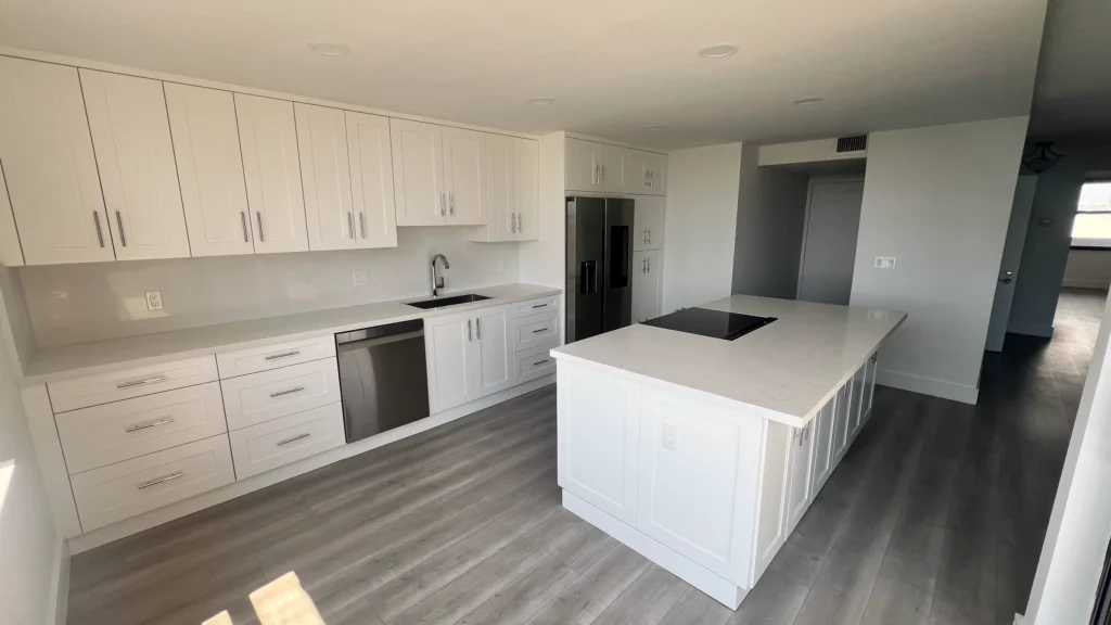 White shaker cabinets along the wall with an island holding a black cooktop