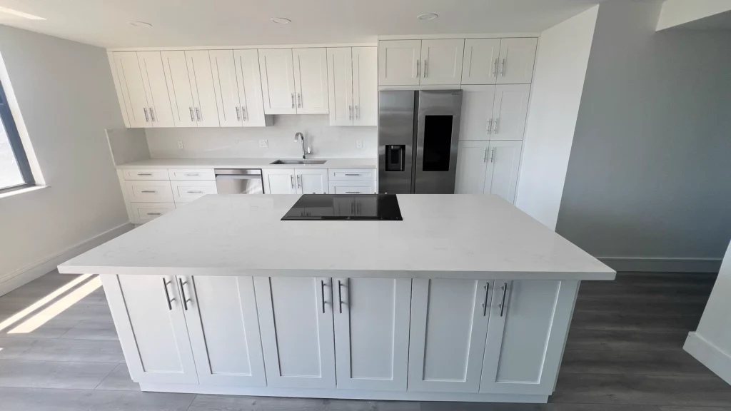 Large white island with a quartz top and cooktop in front of a wall of white cabinets
