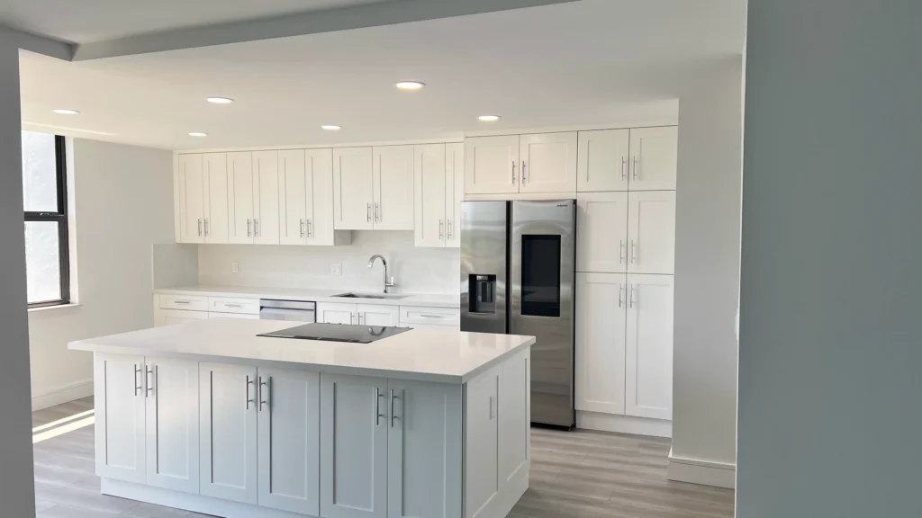 White kitchen with tall pantry cabinets, a stainless refrigerator and an island with sink