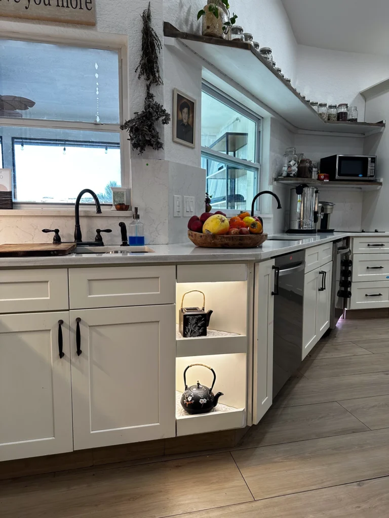 Kitchen sink area with lit open end shelves and floating shelves above the window