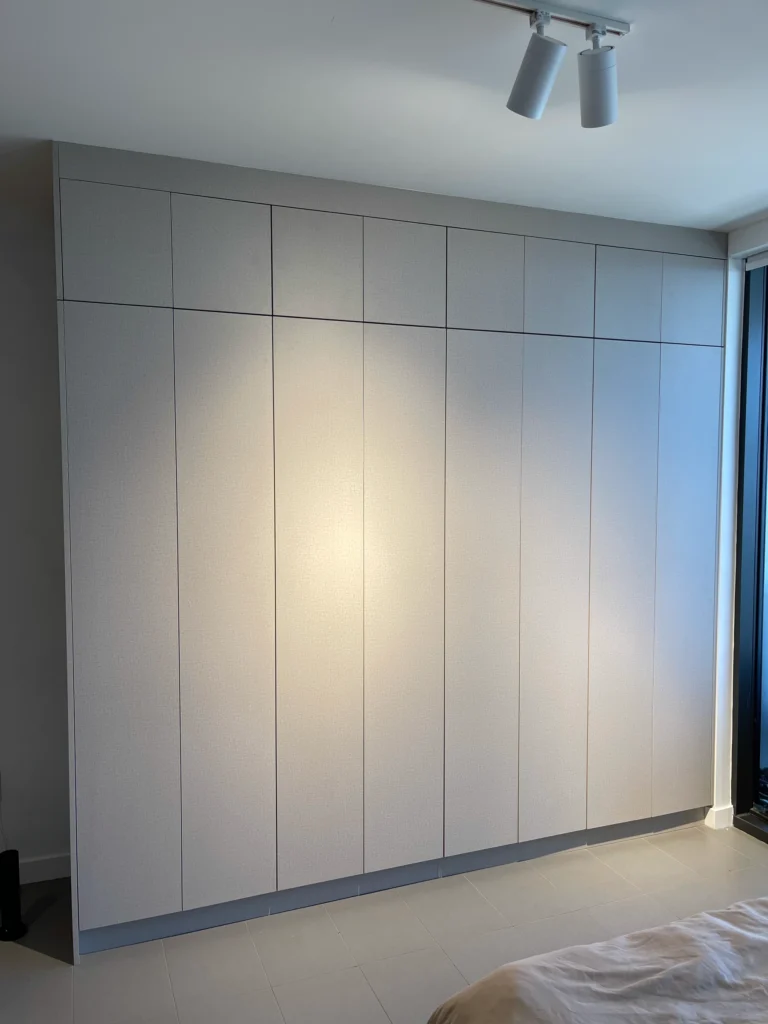 Floor-to-ceiling built-in closet with flat light gray doors in a studio apartment
