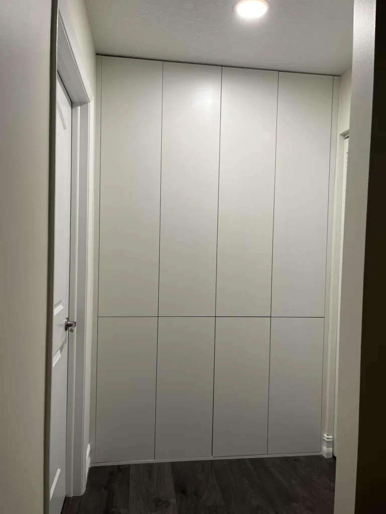 Floor-to-ceiling built-in closet with flat white handleless doors filling a hallway alcove