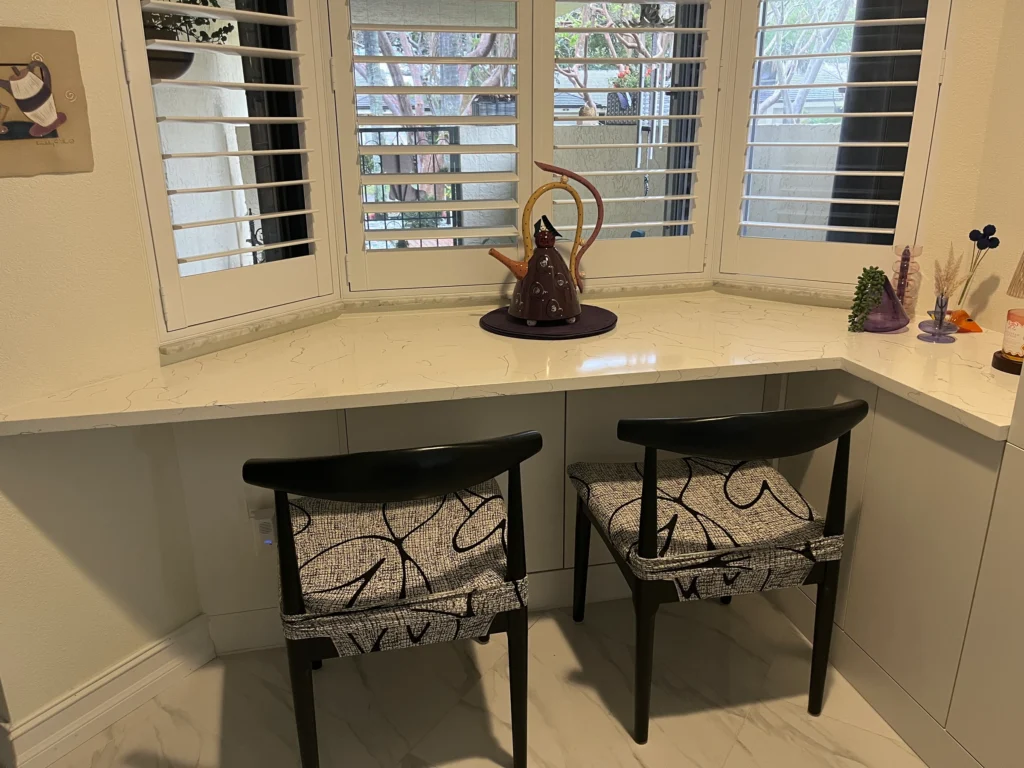 L-shaped quartz counter wrapping a bay window, with two chairs and gray cabinets below