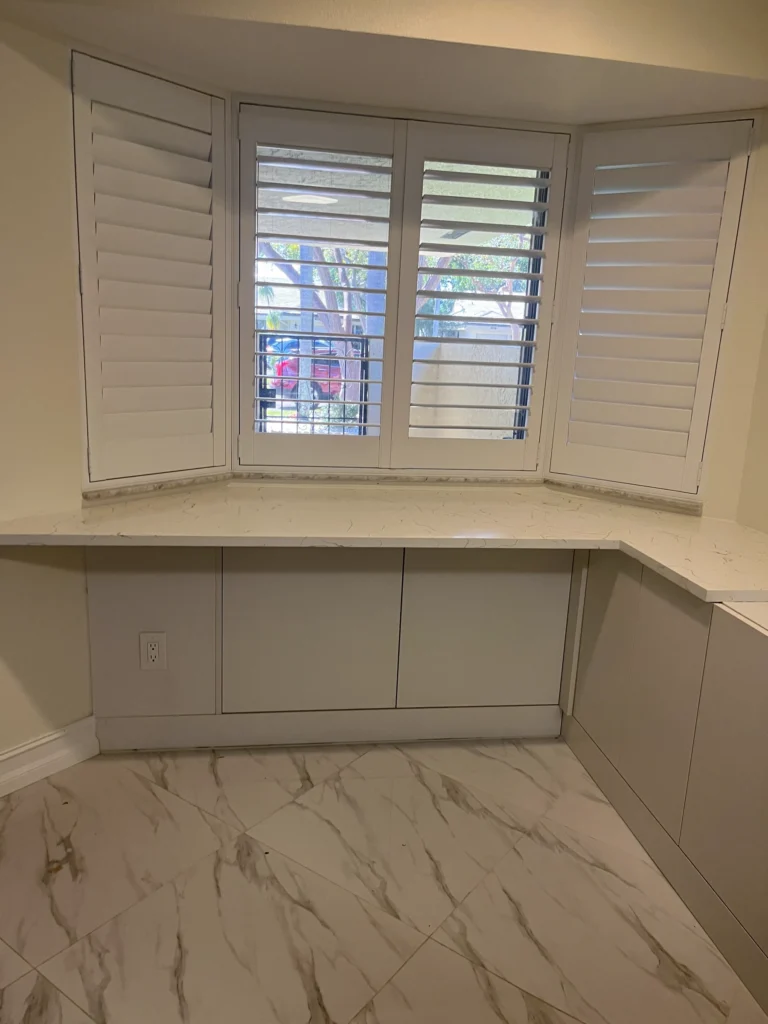 Bay window nook with a quartz counter over flat gray base cabinets and marble-look tile