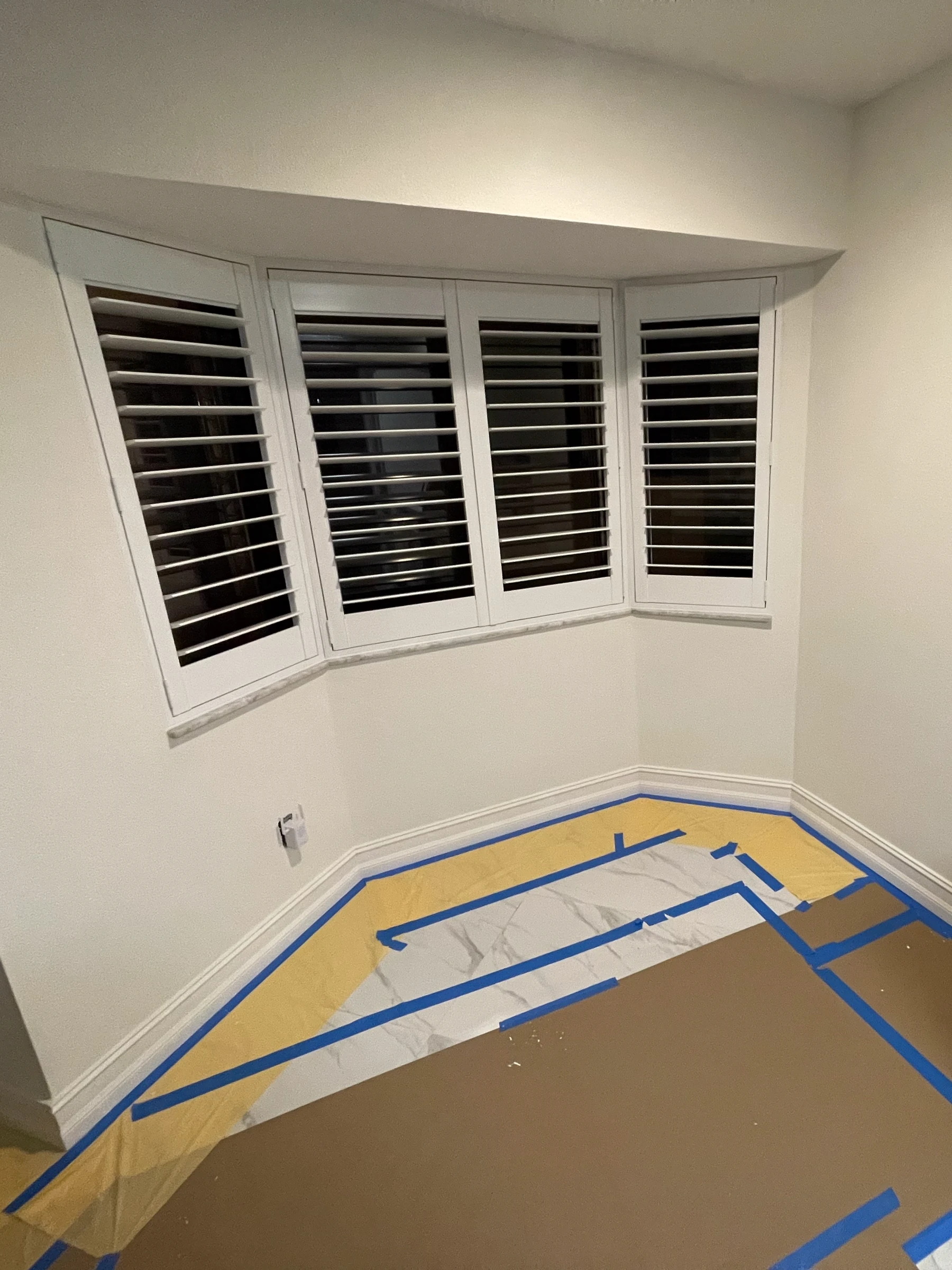 The same bay window nook before, an empty room with the floor covered for protection