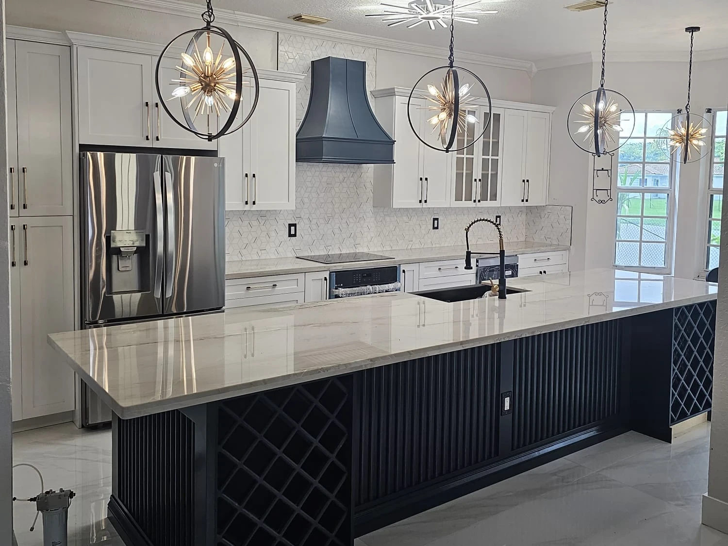 The same kitchen after the redesign, with white shaker cabinets, a navy range hood and a long island