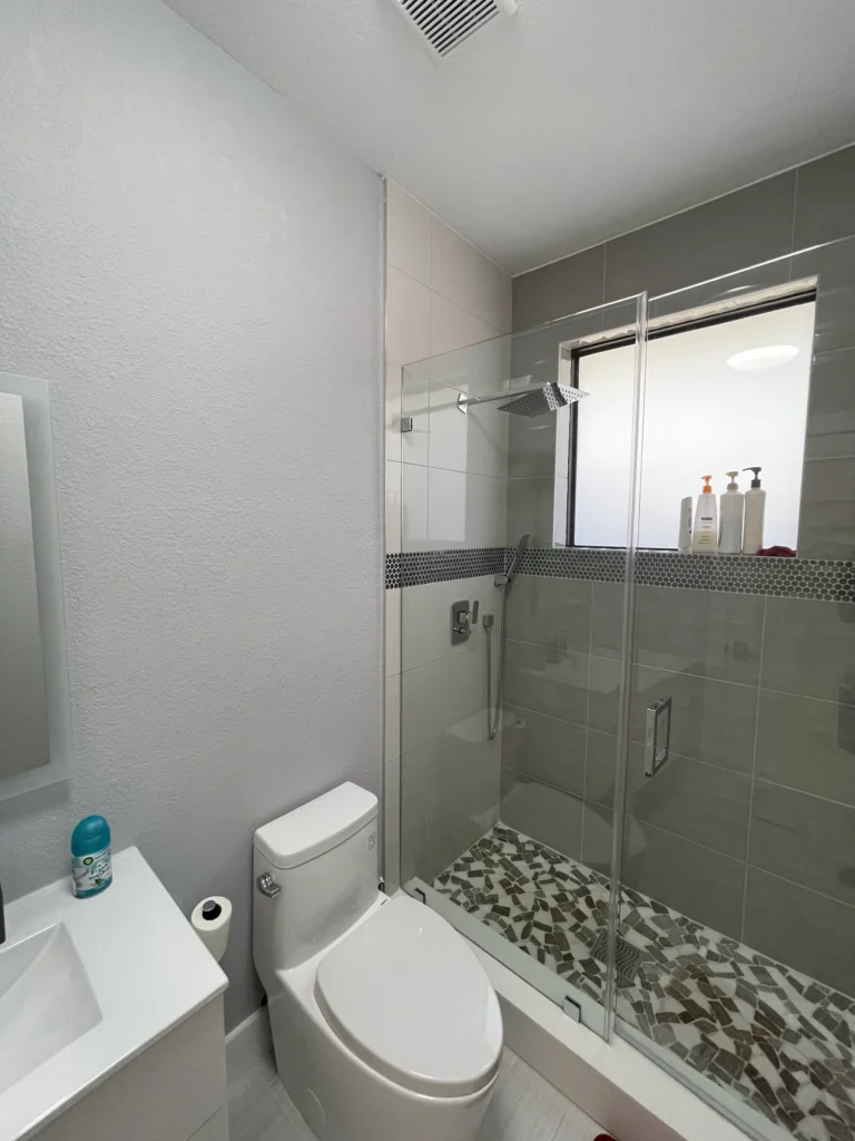 Walk-in shower with glass door and pebble-mosaic floor next to a one-piece toilet
