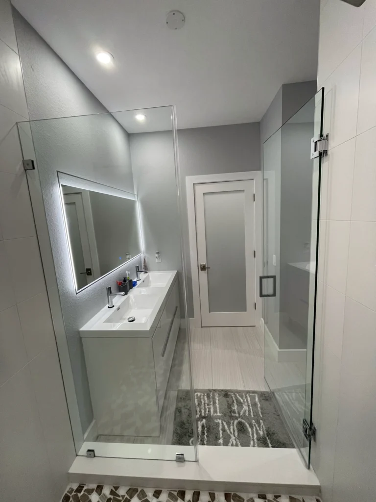 View through a glass shower to the vanity and bathroom door