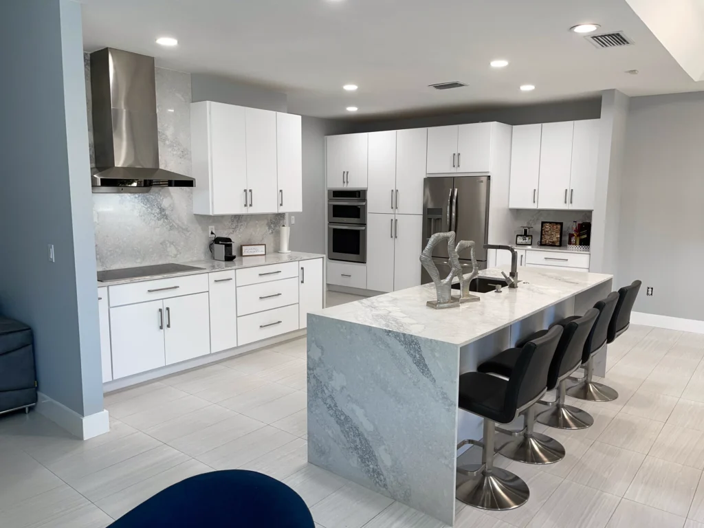 Open white kitchen with a marble-look waterfall island and black bar stools