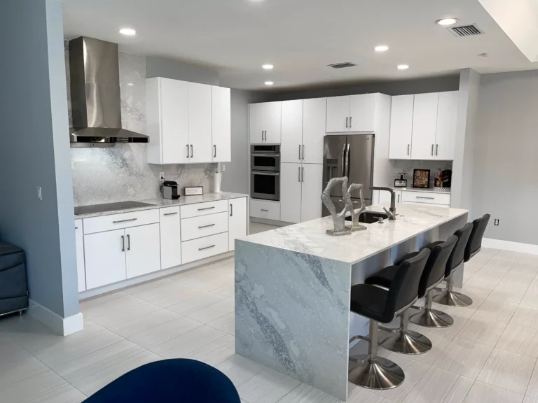 Open white kitchen with a marble-look waterfall island and black bar stools