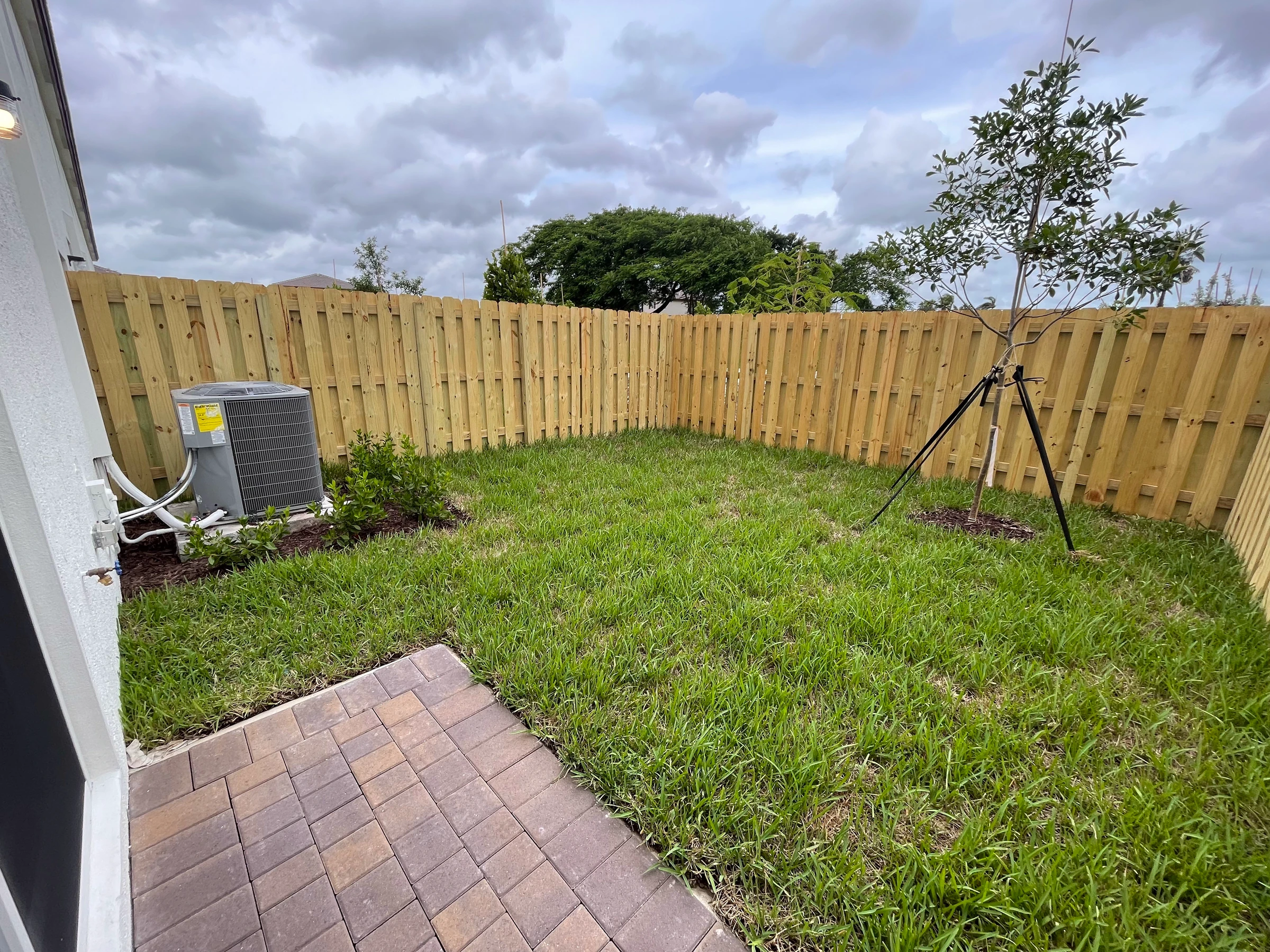 The backyard before the patio: grass, a small paver path and a wood fence