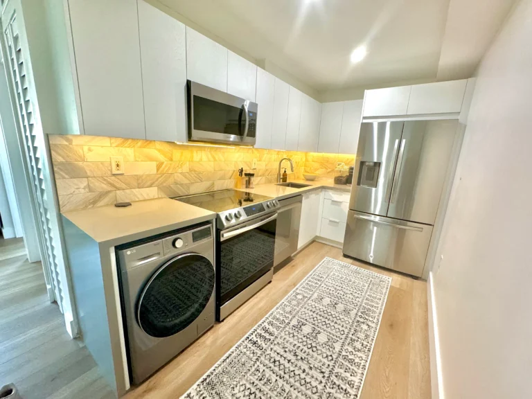 Compact white kitchen with a stone-look backsplash and a washer tucked under the counter