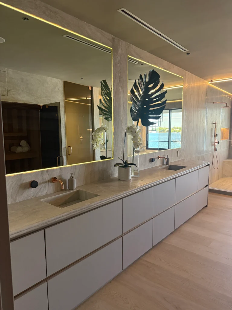 Large bathroom with a long floating vanity, backlit mirrors and stone-look walls