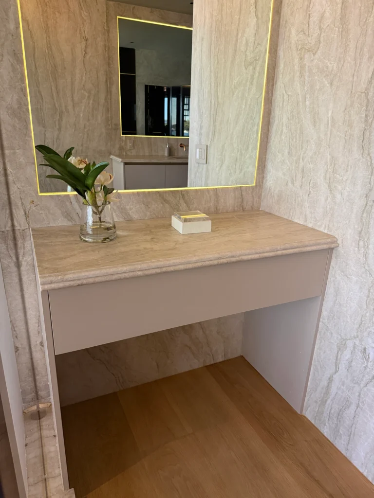 Built-in makeup vanity with a stone top and a backlit mirror