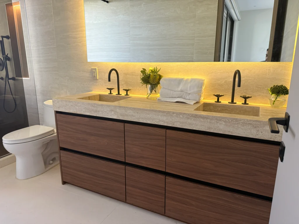 Double walnut vanity with a stone top, two black faucets and a backlit mirror