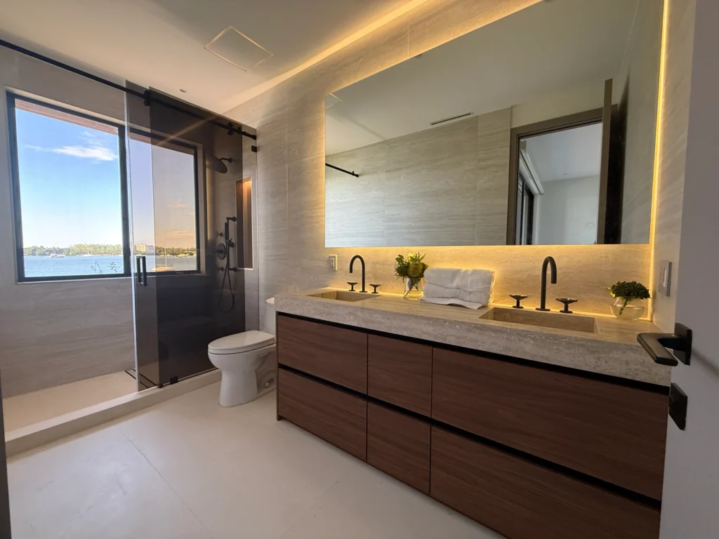 Bathroom with a walnut double vanity, glass shower and a window onto the water