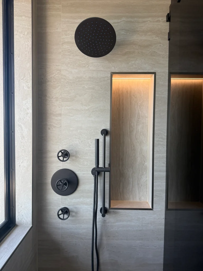 Walk-in shower with a black rain head, lit wall niche and stone-look tile