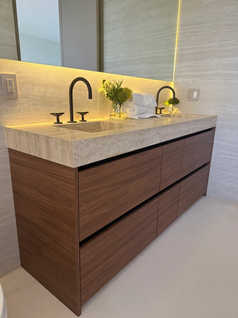 Angled view of a walnut vanity with drawers and a warm under-mirror light