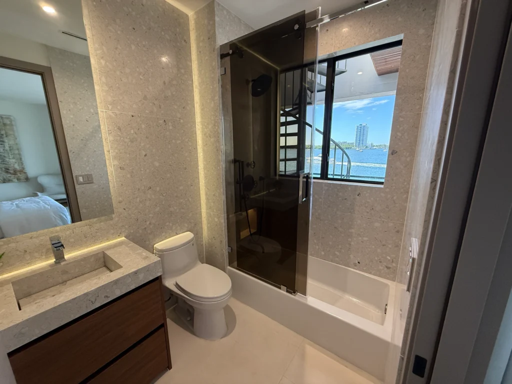 Glass shower with a window view next to a stone sink vanity