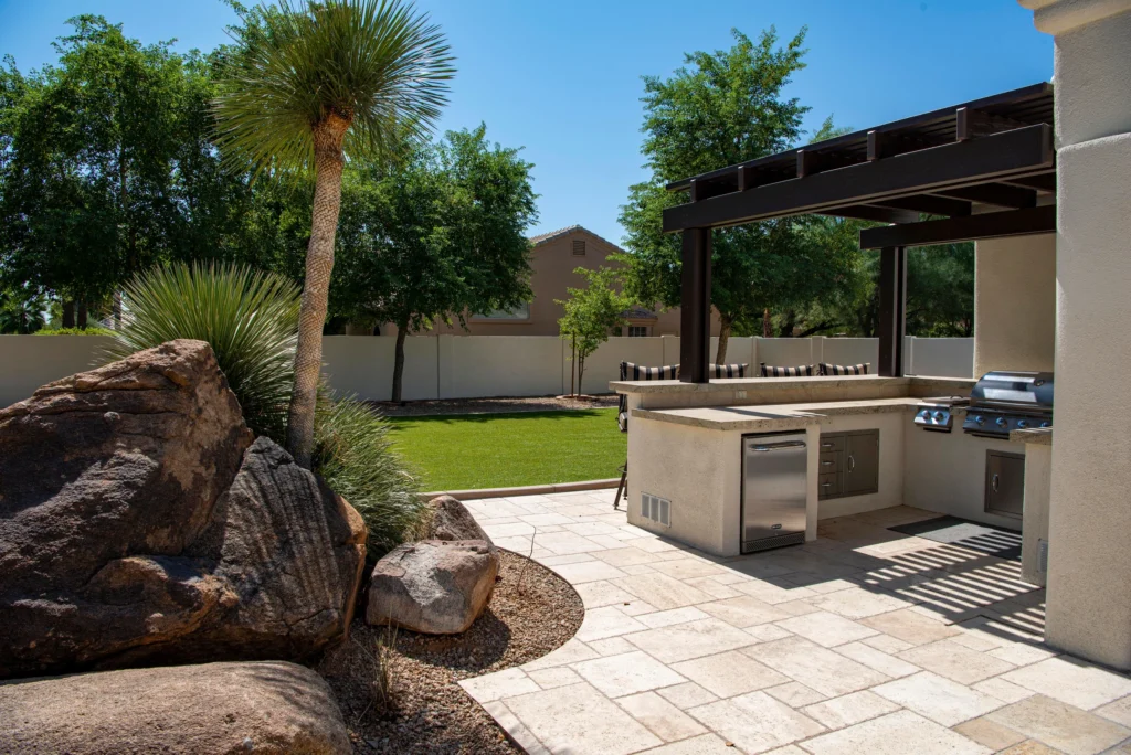 Outdoor kitchen with grill under a pergola beside a paved patio