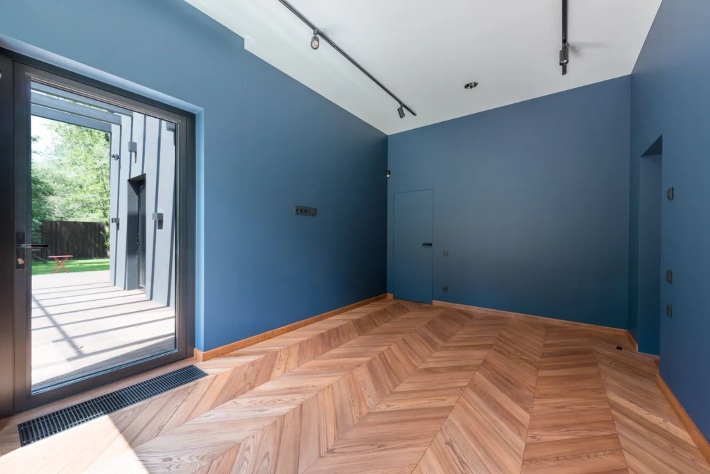 Herringbone wood floor in an empty room with a glass door to the garden