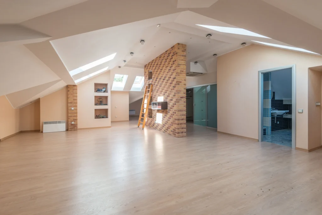 Open loft room with skylights, light wood floor and a brick accent column