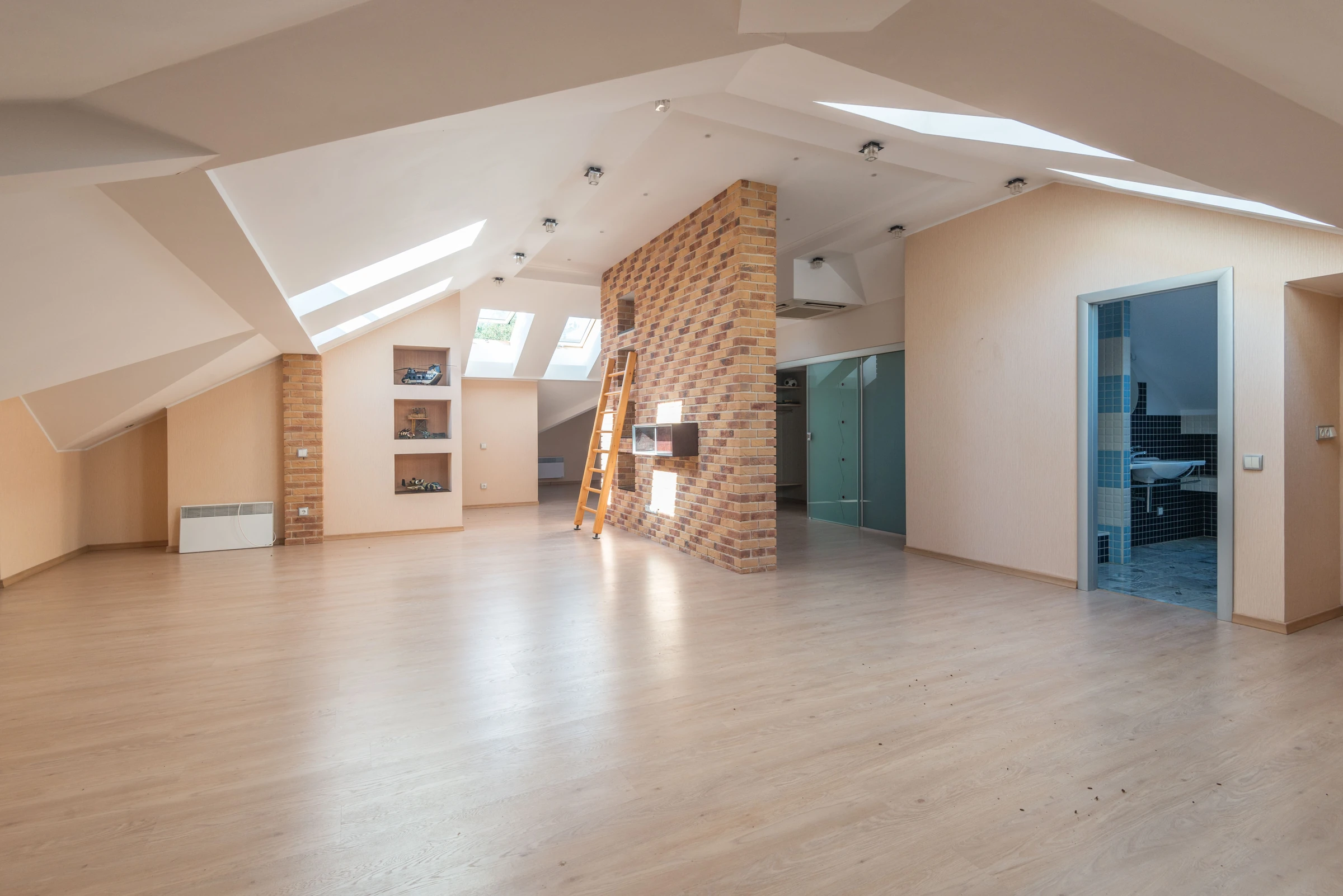 Open loft room with skylights, light wood floor and a brick accent column
