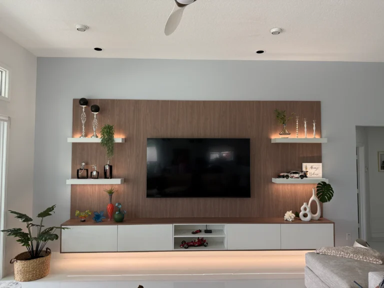 Custom TV wall with a walnut back panel, lit floating shelves and a long white media console