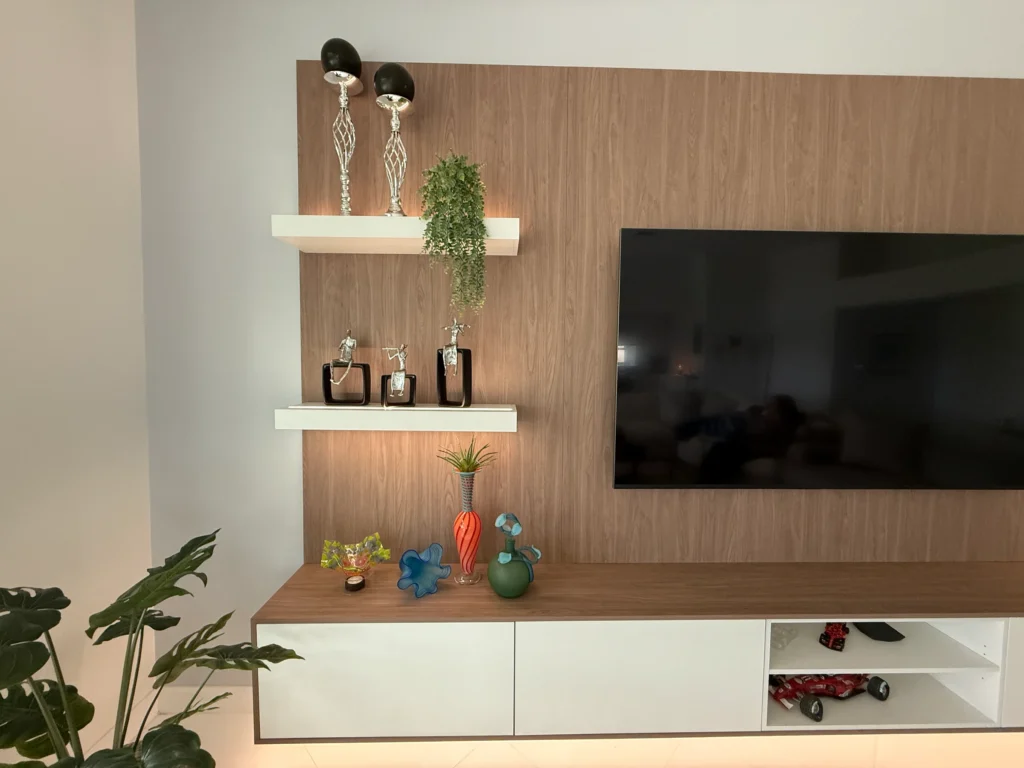 The walnut panel with two lit floating shelves beside the mounted TV