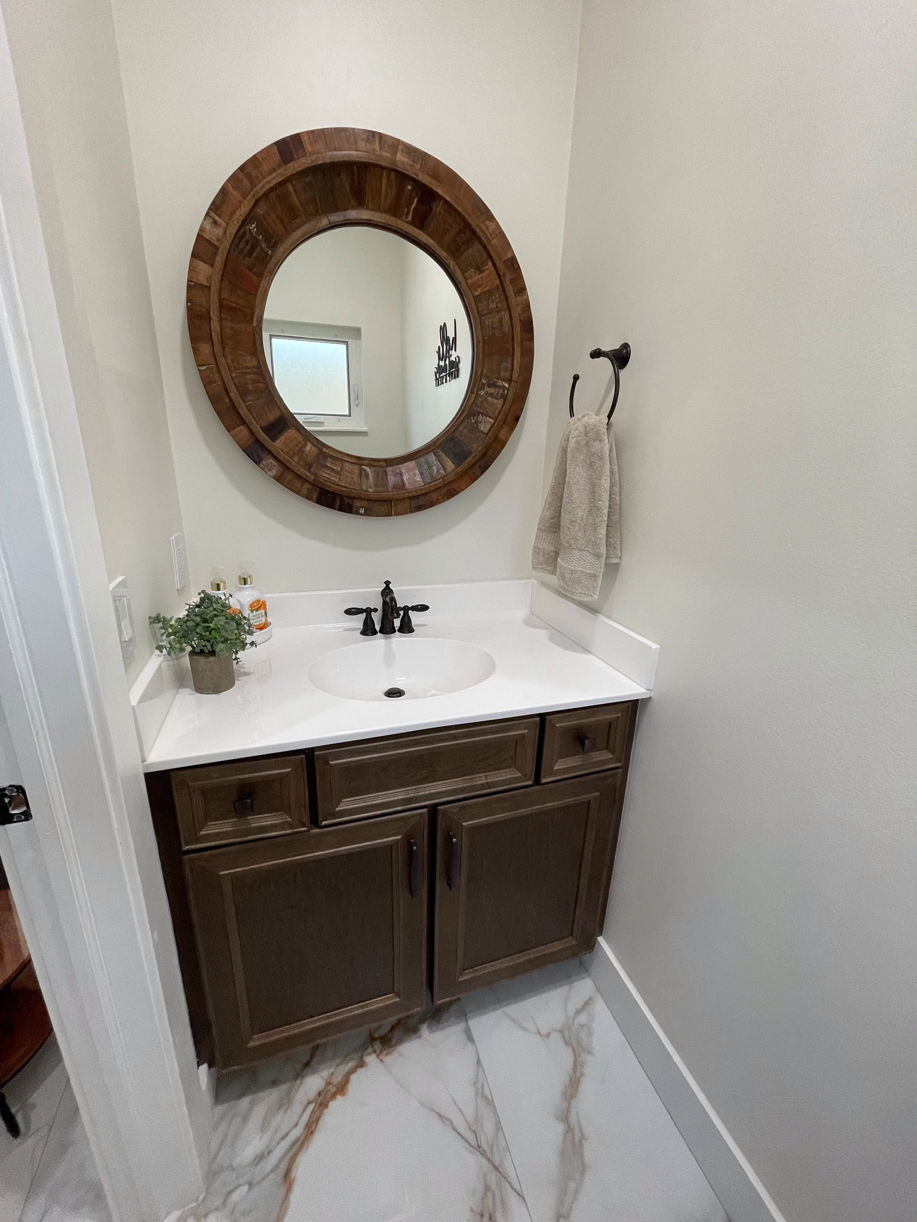 Guest bathroom with a dark wood vanity, white top and round wood-frame mirror