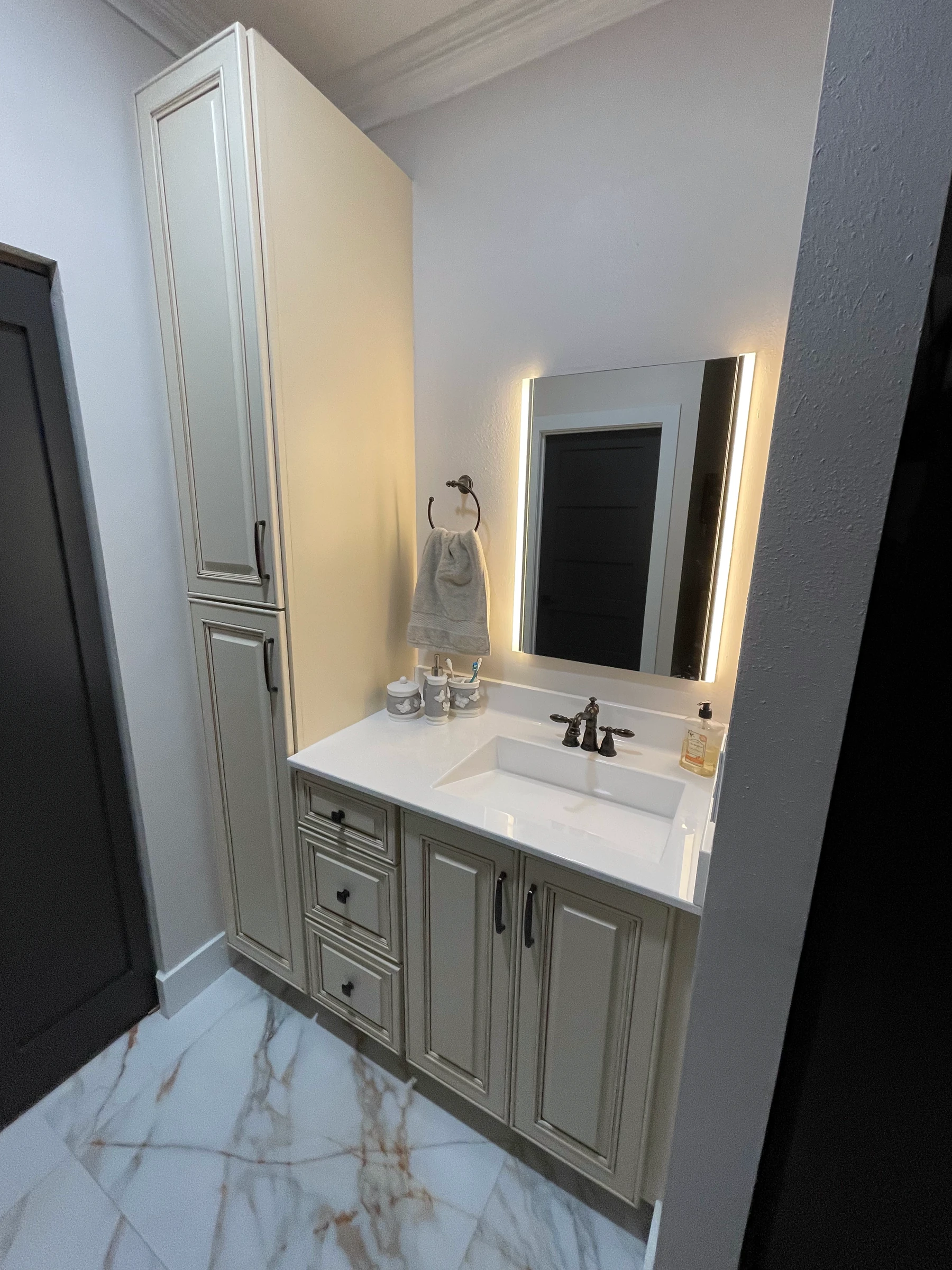 Master bathroom with a linen tower, antique white vanity and backlit mirror