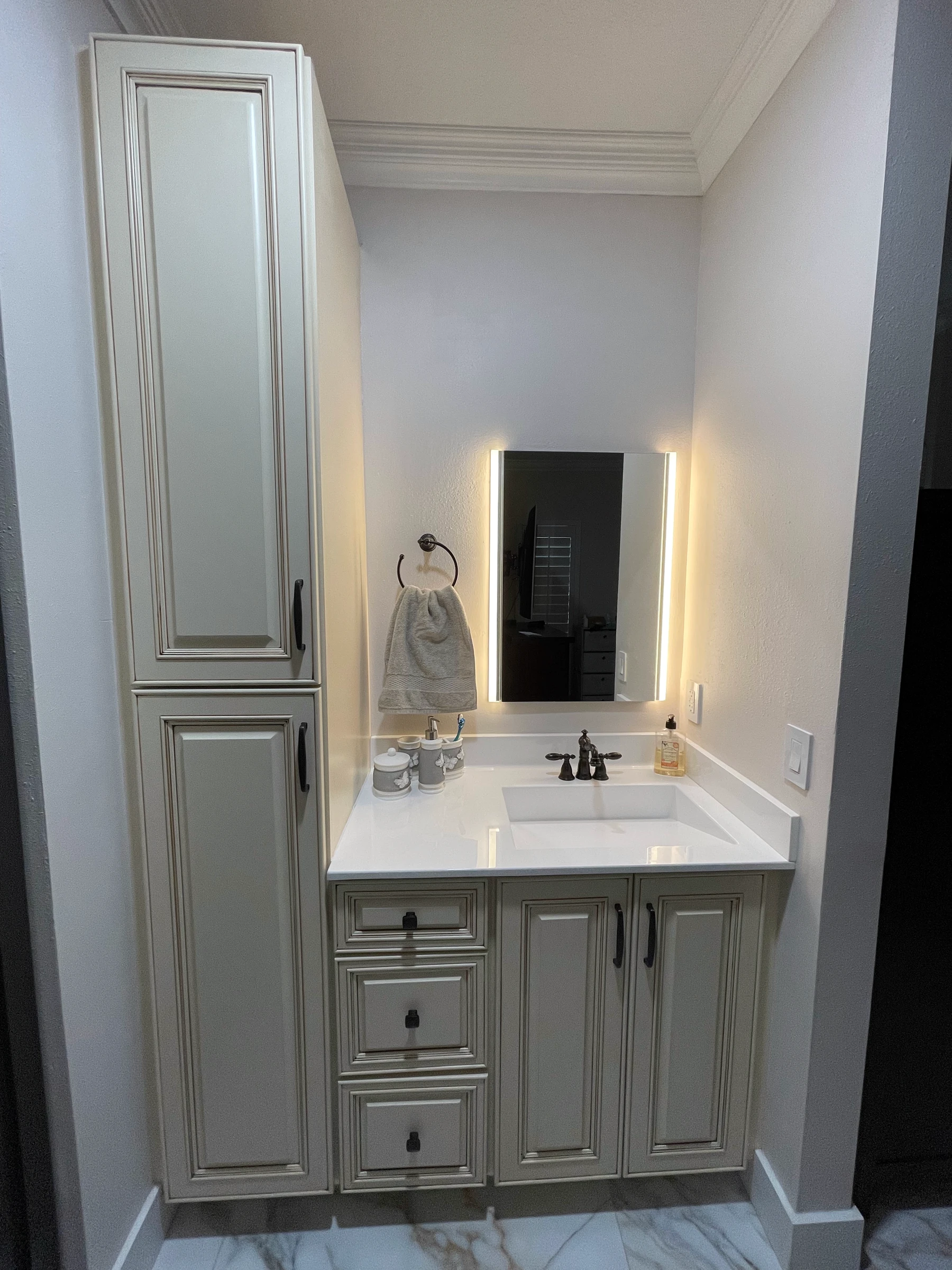 Tall linen cabinet beside a vanity with oil-rubbed bronze faucet