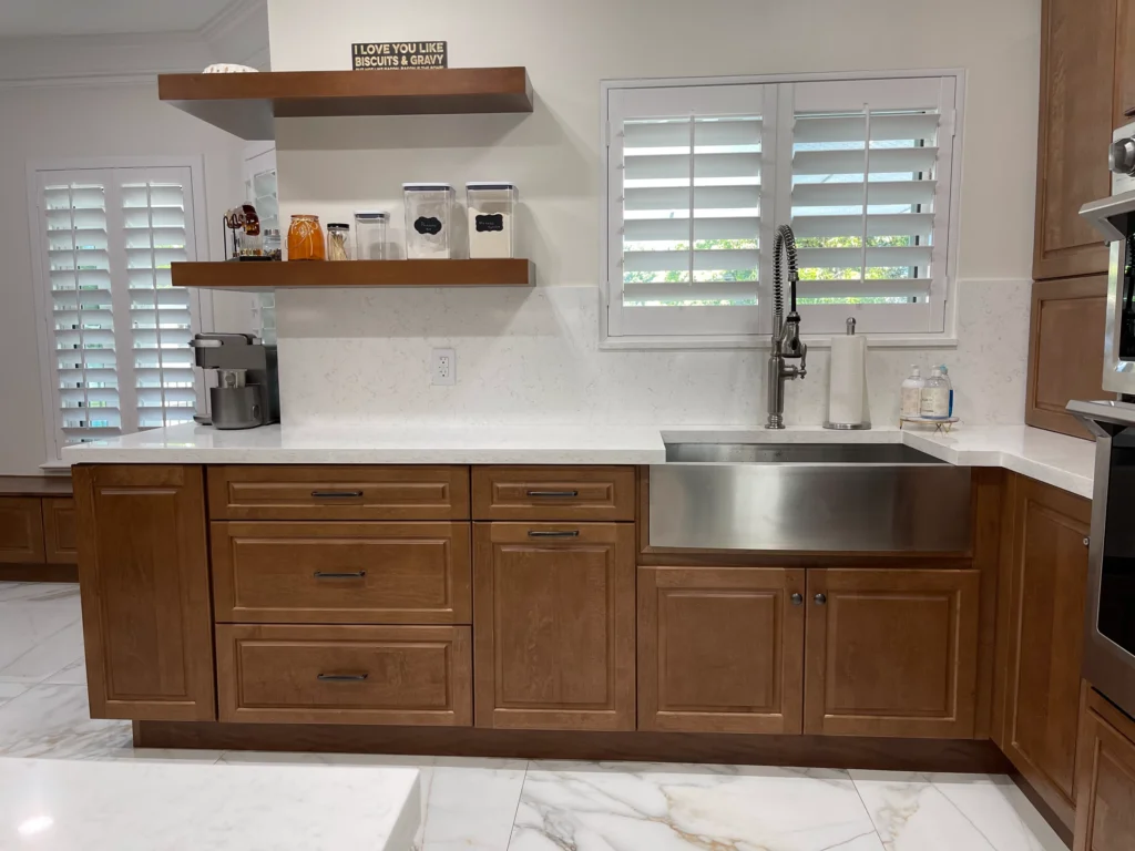 Farmhouse sink under a shuttered window with floating wood shelves