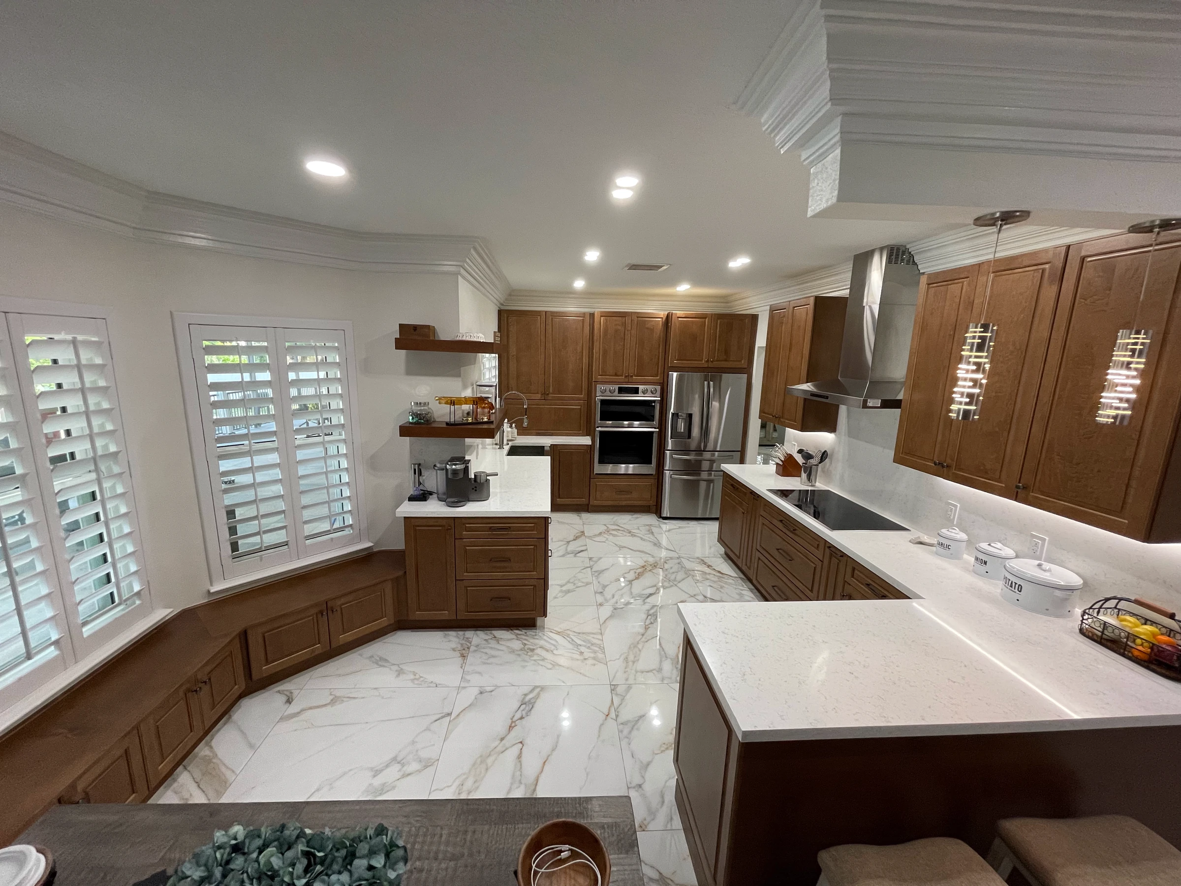 Full view of a wood and white kitchen with window seat and marble-look floor