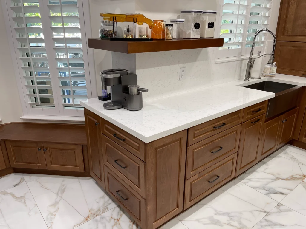 Corner of wood cabinets with white quartz top, farmhouse sink and floating shelf