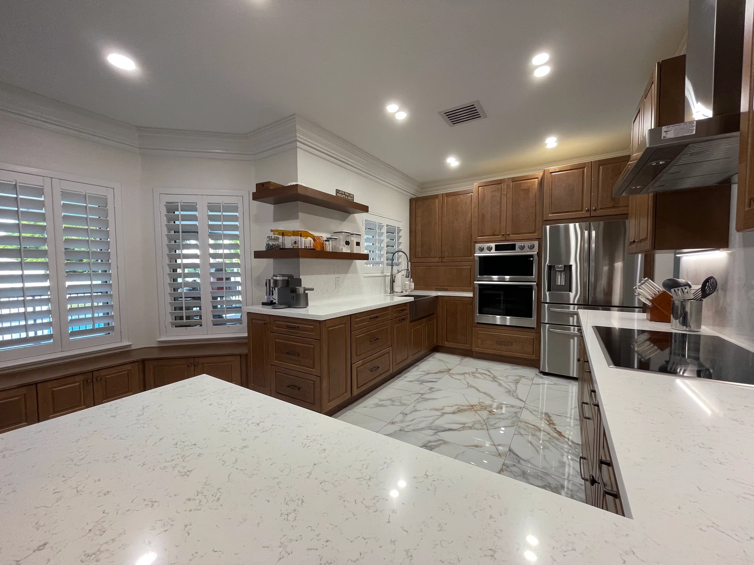 Wood kitchen with floating shelves, wall ovens and a quartz peninsula